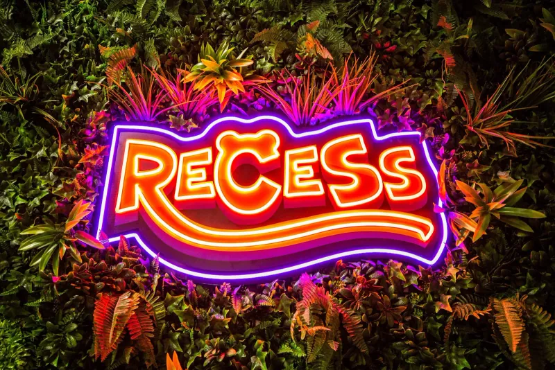The illuminated Recess sign set into a green foliage wall